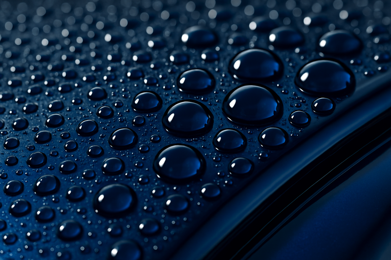 A dramatic close-up, macro photo of water beading perfectly into tight, spherical drops on the hood of a deep blue car. The paint is extremely glossy, demonstrating the hydrophobic effect of a ceramic sealant.